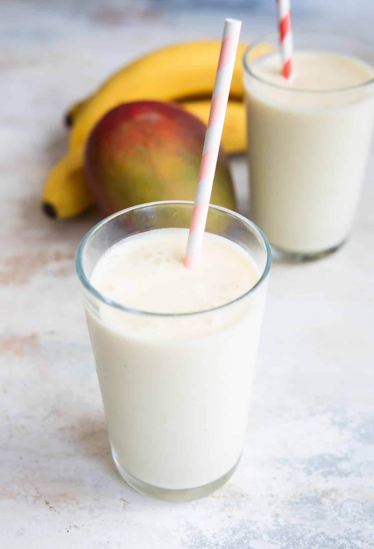 Two glasses of mango smoothie next to a mango and some bananas.
