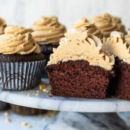 A cake stand filled with chocolate cupcakes with peanut butter frosting, 1 cut open to show the inside.