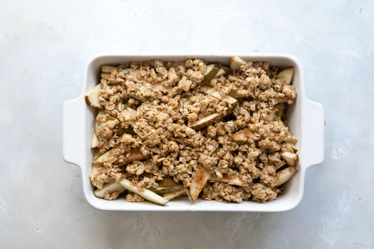 An unbaked pear crisp in a white baking dish.