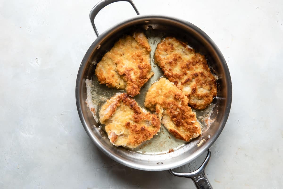 Pork tenderloin cutlets fried in a skillet of oil.