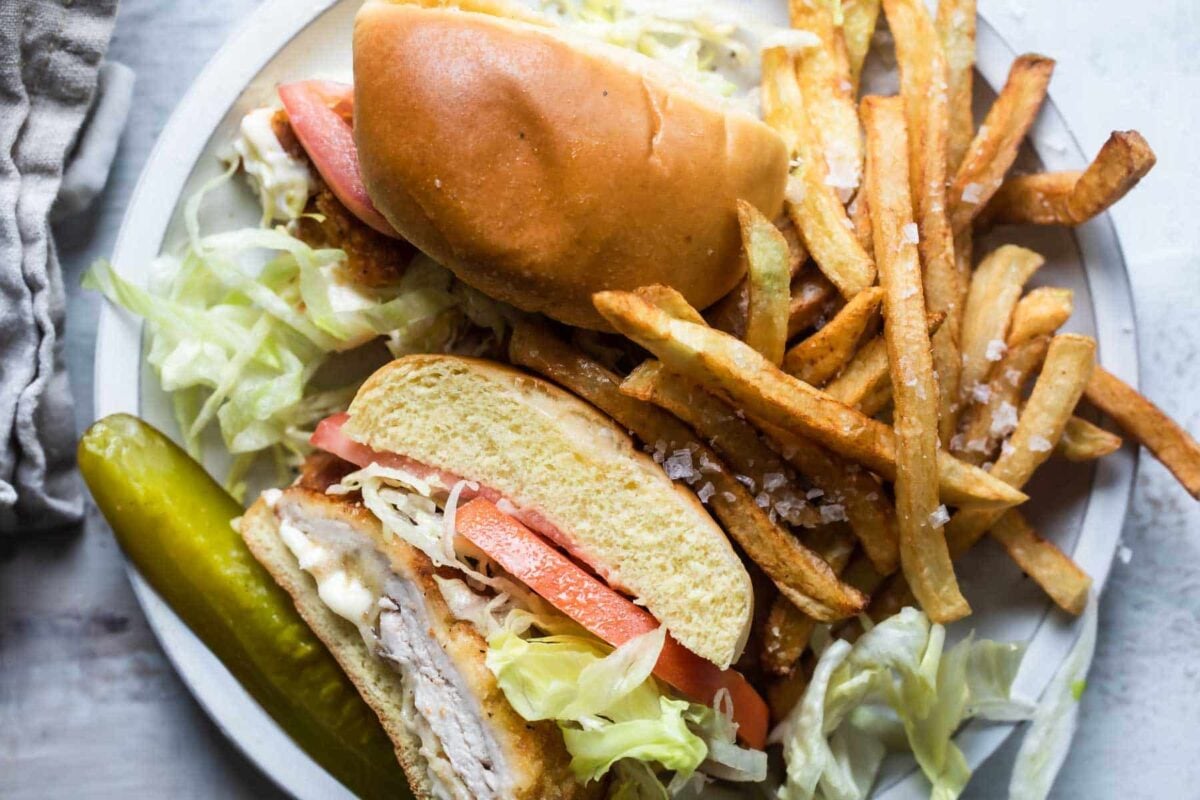 A pork tenderloin sandwich on a plate with french fries.