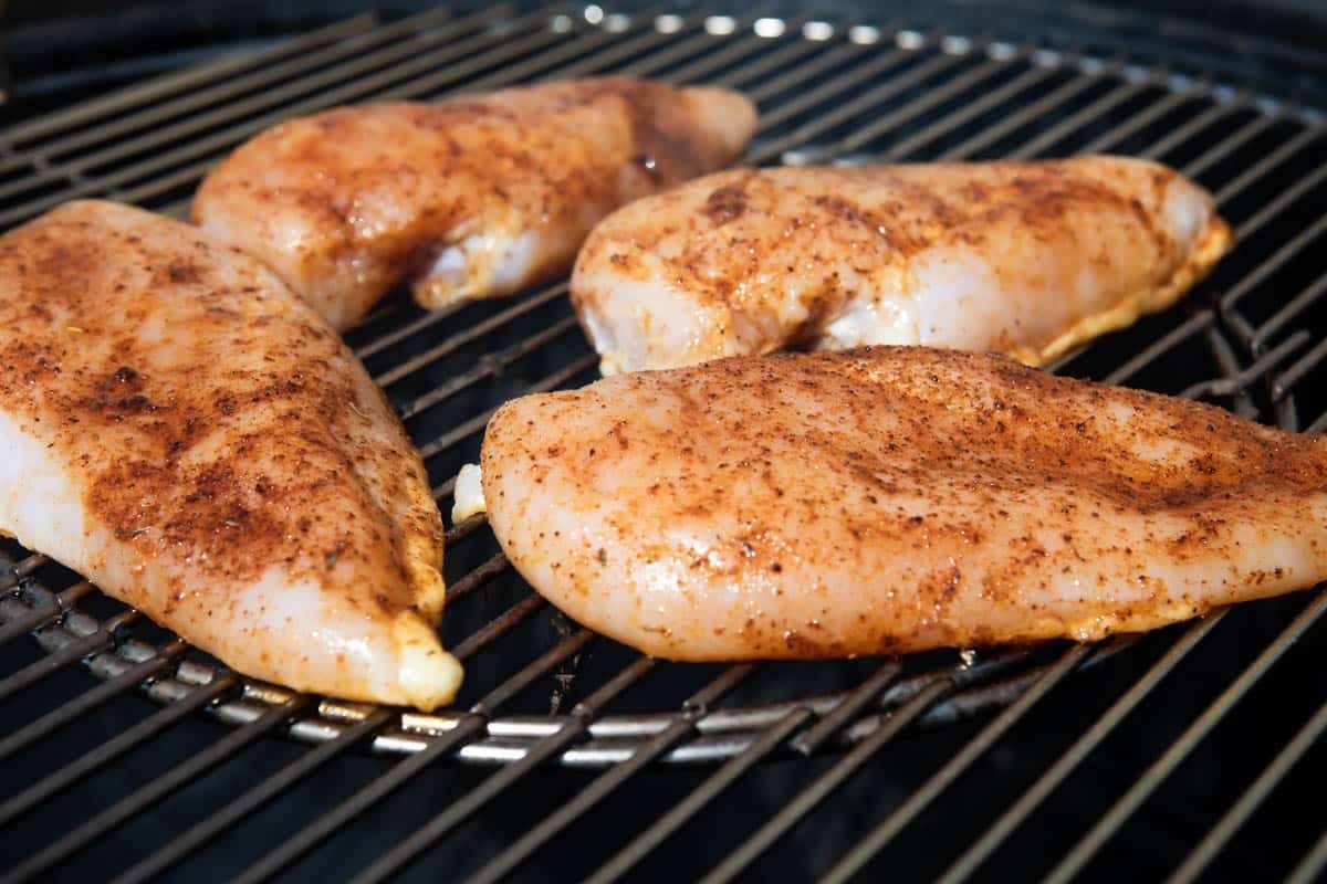 An angled shot of uncooked chicken breasts on a smoker.