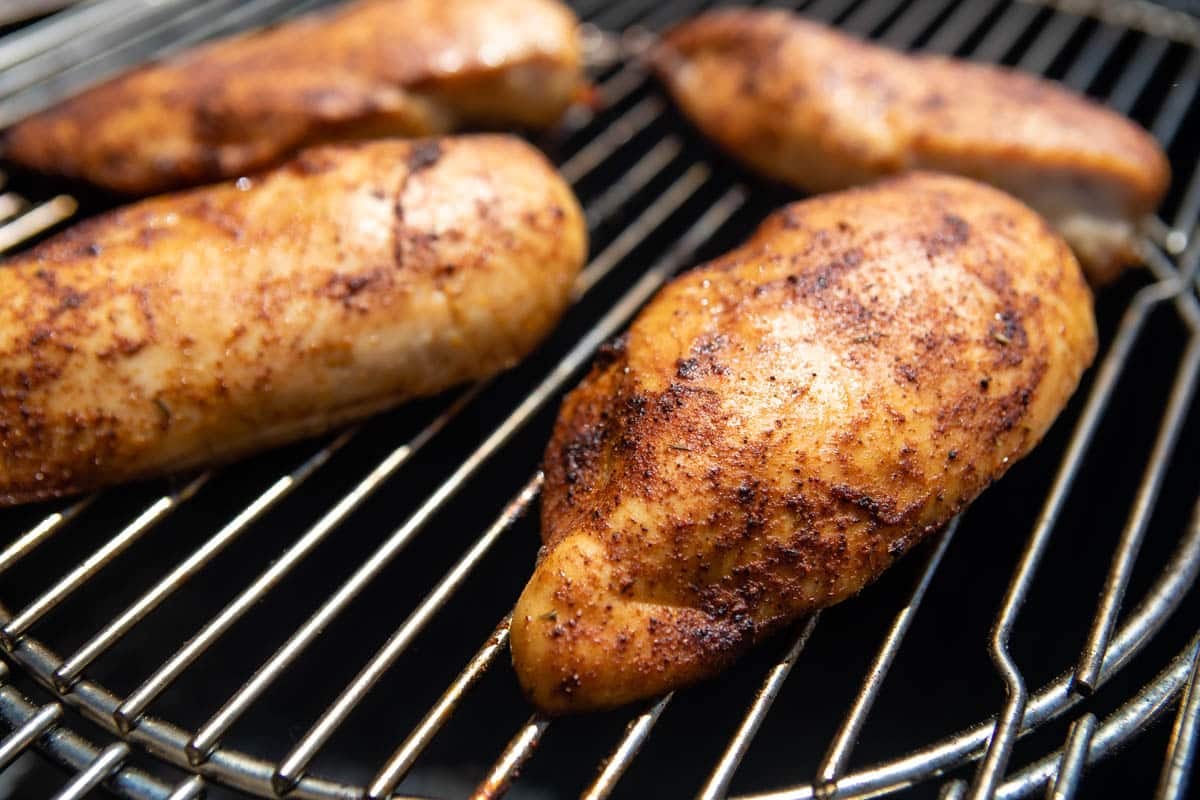 A side shot of cooked chicken breasts on a smoker.