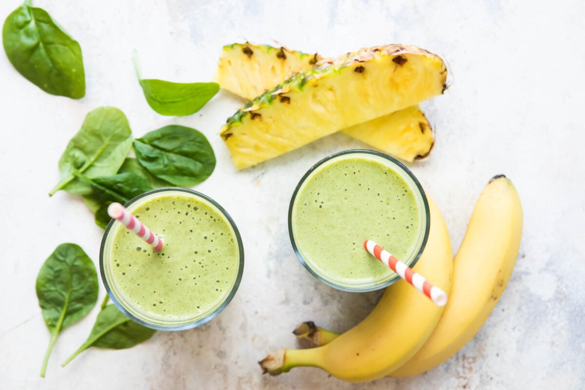 2 glasses of Spinach Smoothie with ingredients nearby.