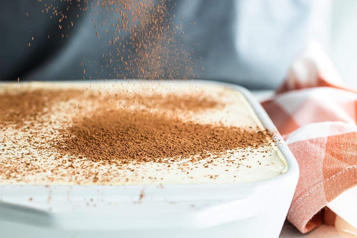 Tiramisu being dusted with cocoa powder.
