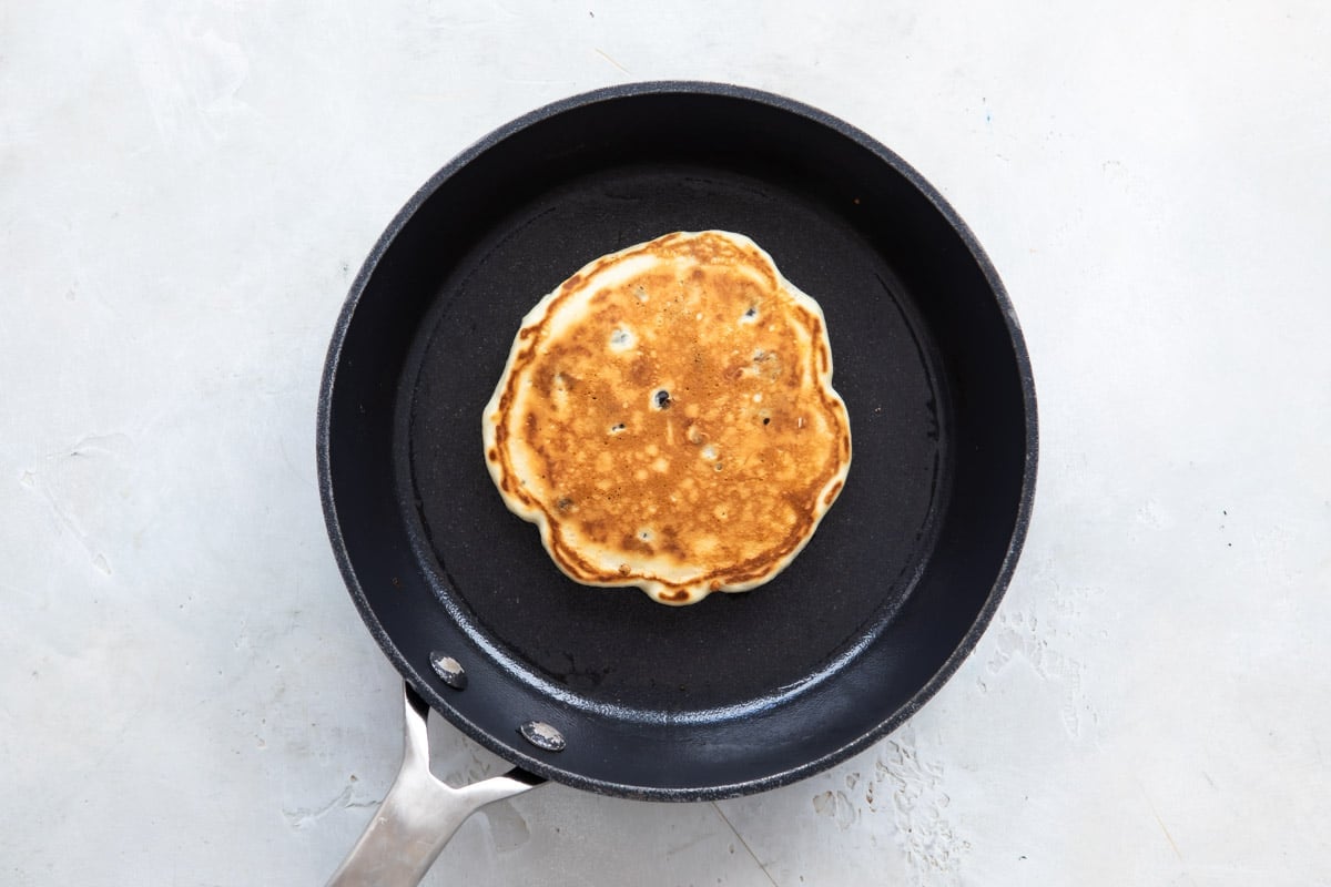 A Pancake in a skillet after flipping so cooked side is up.