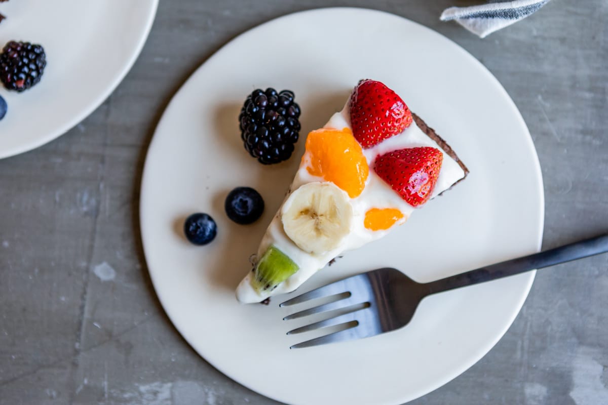 A slice of brownie pizza on a white plate with a fork.