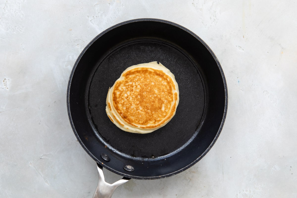 A Pancake in a skillet after flipping so cooked side is up.