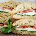 A stack of Caprese Sandwiches on a wooden cutting board.