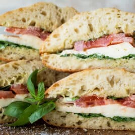 A stack of Caprese Sandwiches on a wooden cutting board.