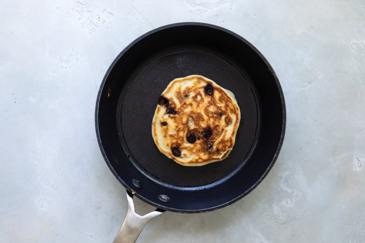 A Pancake in a skillet after flipping so cooked side is up.