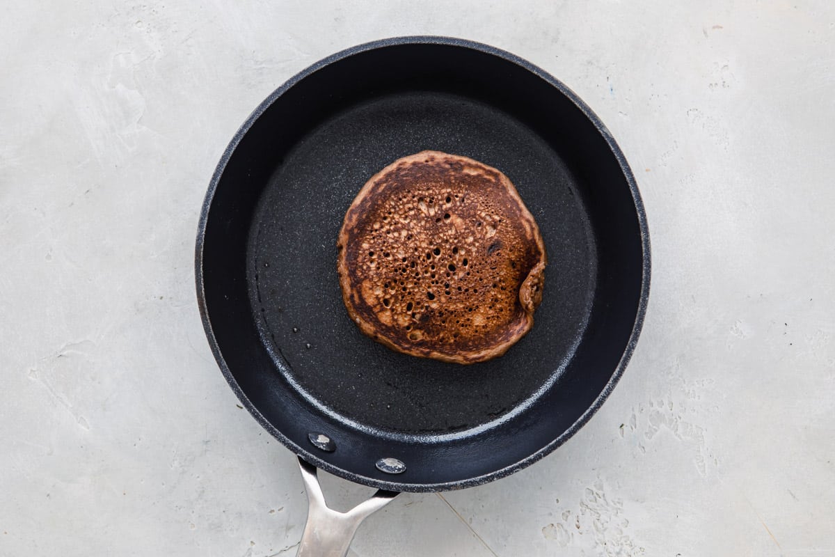 A Pancake in a skillet after flipping so cooked side is up.