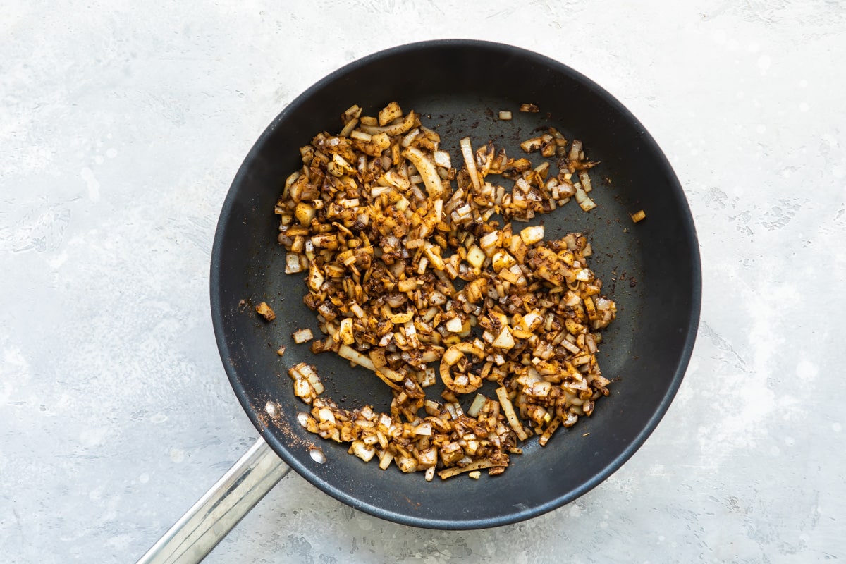 A skillet with onions and spices cooking in it.