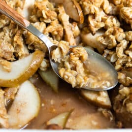 Pear crisp in a baking dish with a spoon resting in it.