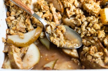 Pear crisp in a baking dish with a spoon resting in it.