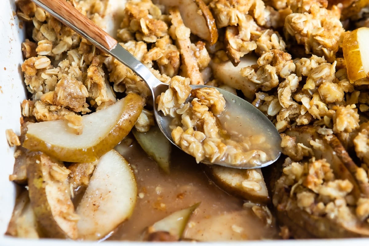 Pear crisp in a baking dish with a spoon resting in it.