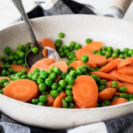 Peas and carrots in a white frying pan.