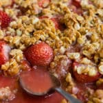 A baking dish of strawberry crisp with a spoon resting in it.