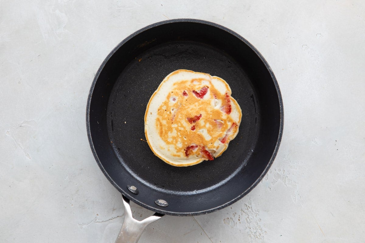 A Pancake in a skillet after flipping so cooked side is up.