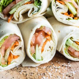 A pile of veggie wraps cut open on a cutting board.