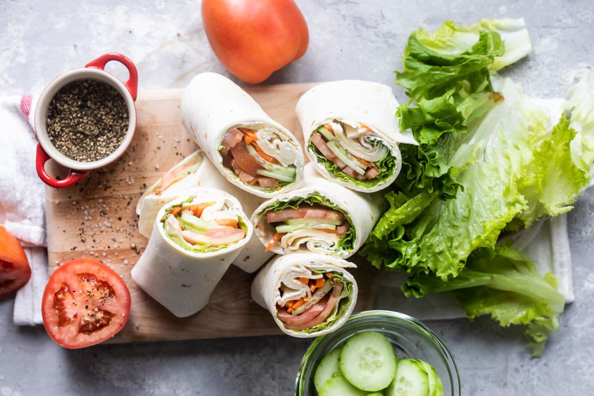 A pile of veggie wraps cut open on a cutting board.