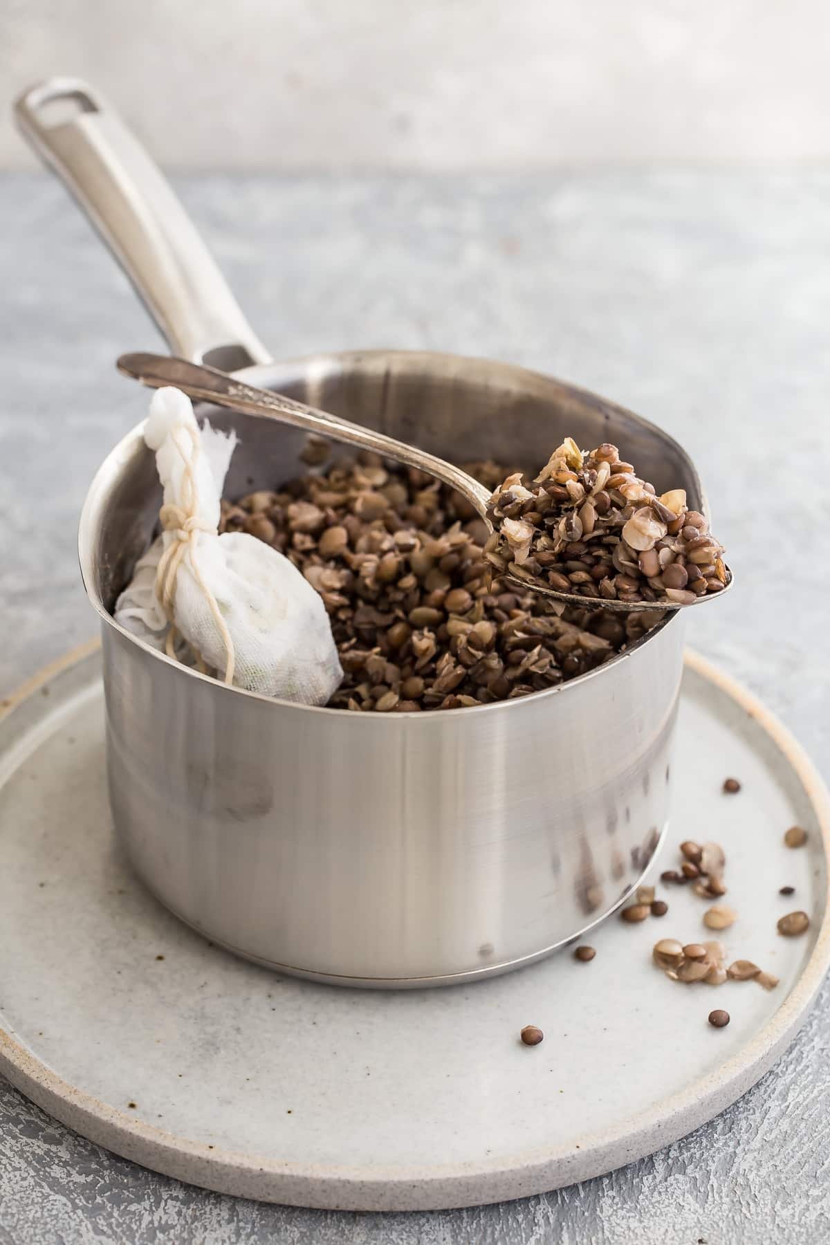 Cooked lentils in a silver pot with some in a spoon resting on the edge of the pot.