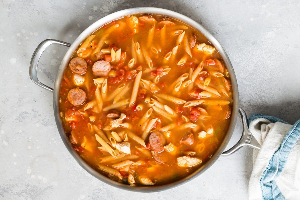 Adding pasta to a skillet of Cajun Pasta.
