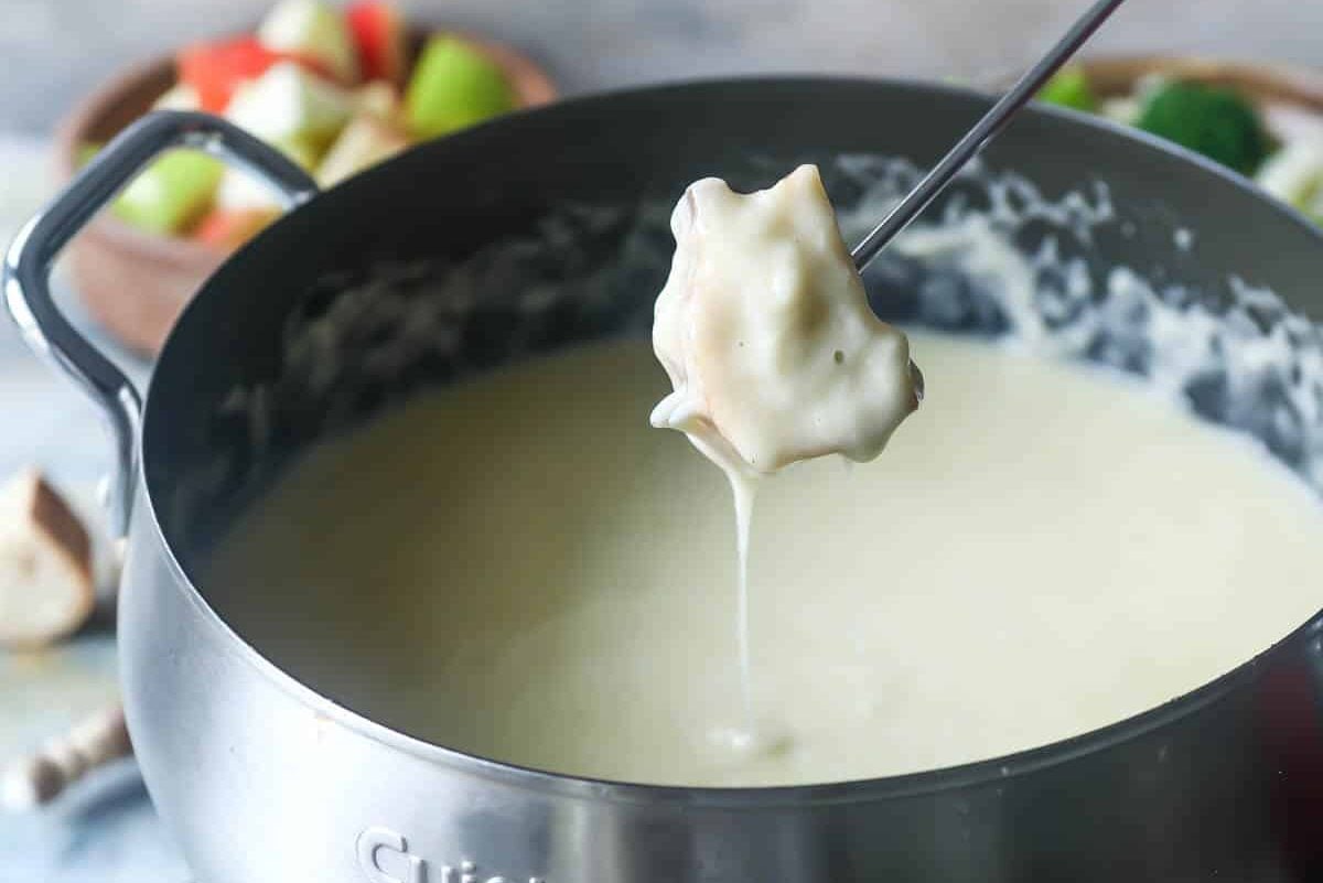 A pot of cheese fondue surrounded by bread and vegetables for dipping.