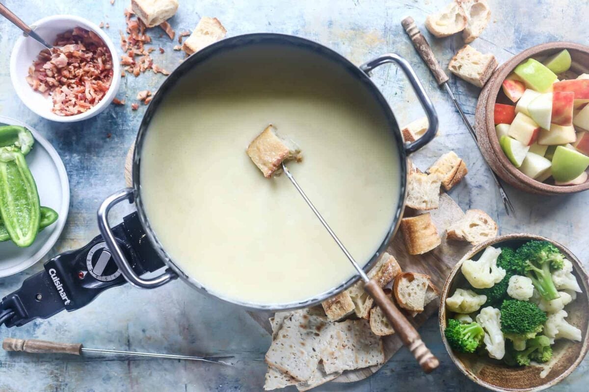 A pot of cheese fondue surrounded by bread and vegetables for dipping.