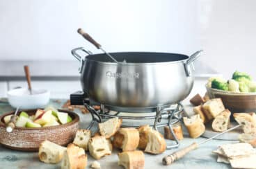 A pot of cheese fondue surrounded by bread and vegetables for dipping.