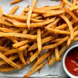 Homemade french fries on parchment paper next to a small cup of ketchup.