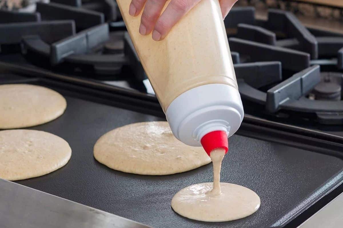 Person holding pancake dispenser over a griddle and dispensing batter