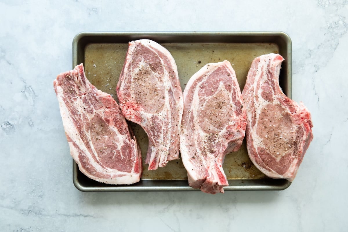 Four bone-in porkchops on a baking sheet.