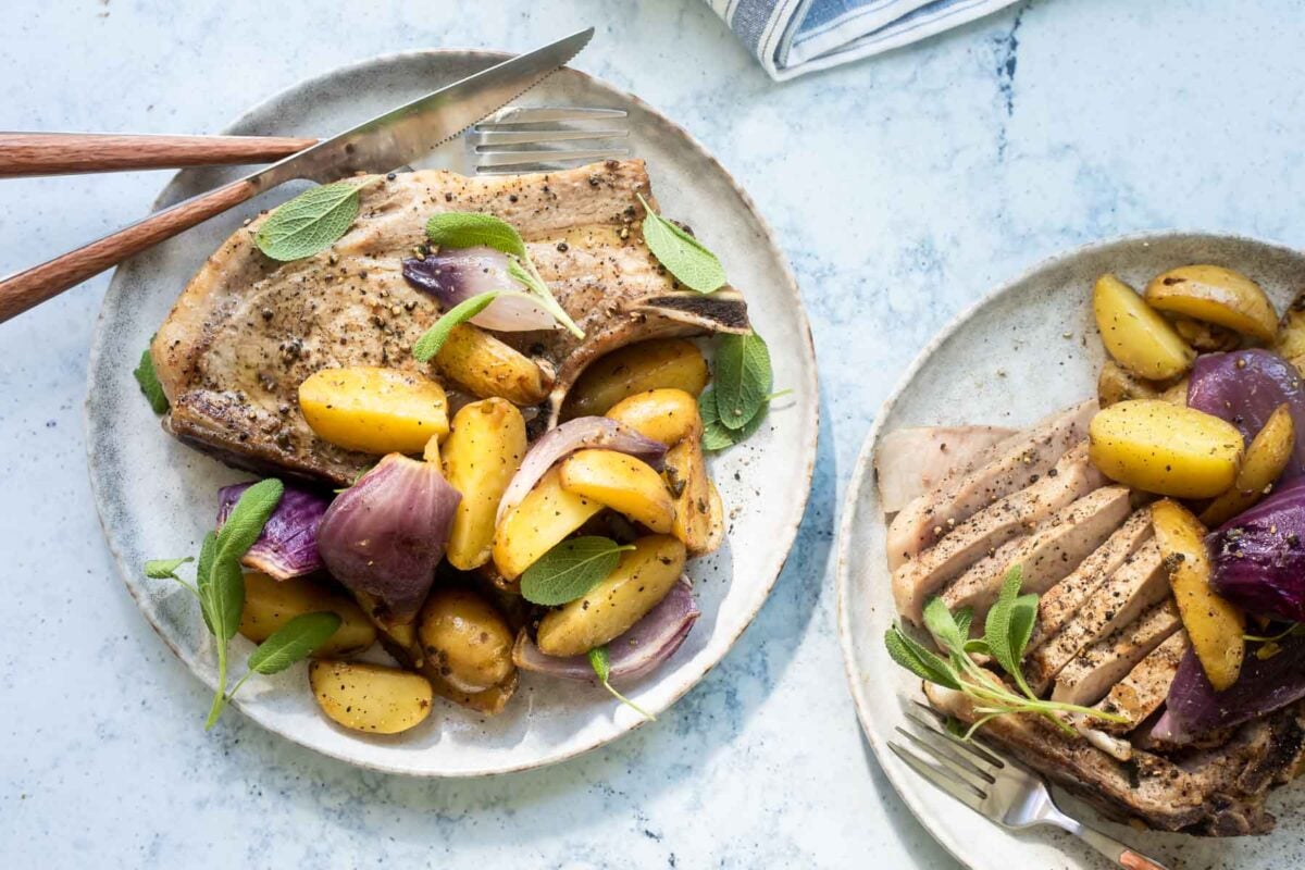 Two plates with baked pork chops, silverware, and vegetables.