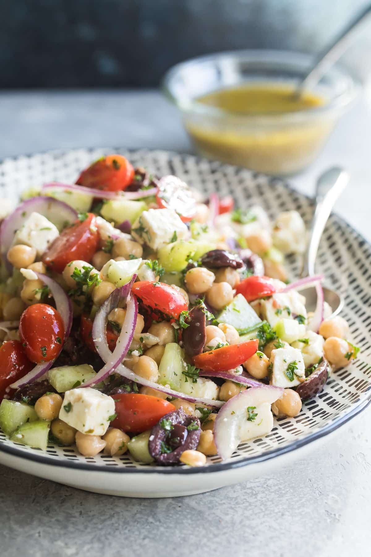 Chickpea salad on a black and white serving platter with a spoon resting in it.
