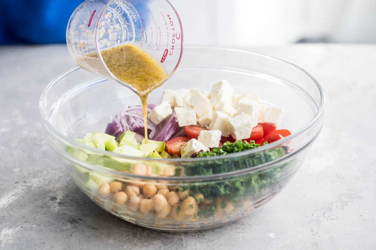 Dressing being poured onto chickpea salad ingredients.