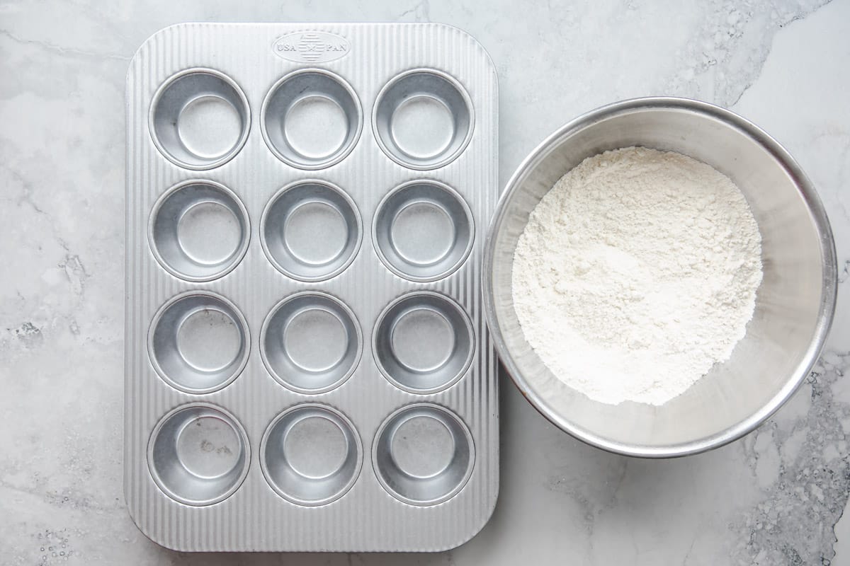 An empty muffin pan next to a bowl of dry muffin ingredients.