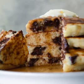 A stack of four chocolate chip pancakes on a plate.