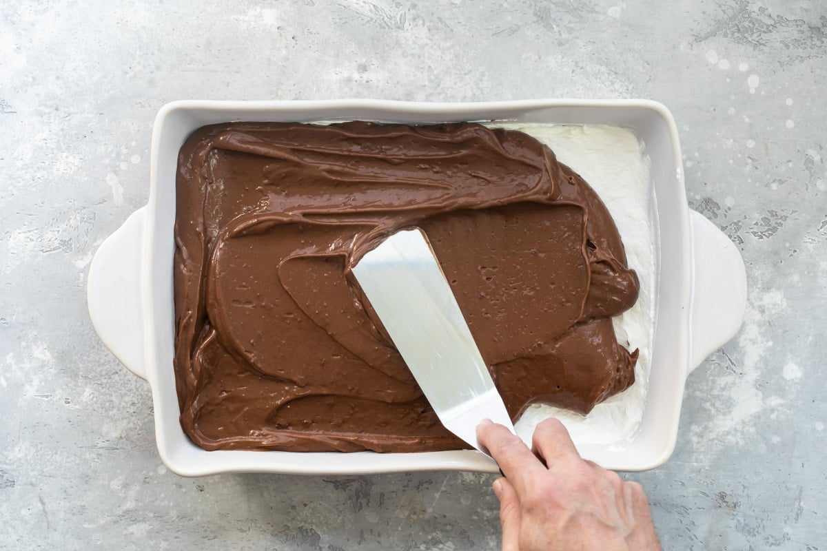 The chocolate layer of chocolate lasagna being added to a white baking dish.