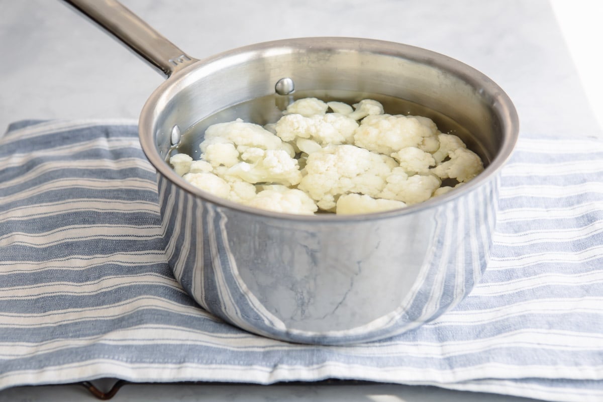 Cauliflower florets soaking in water in a metal sauce pan.