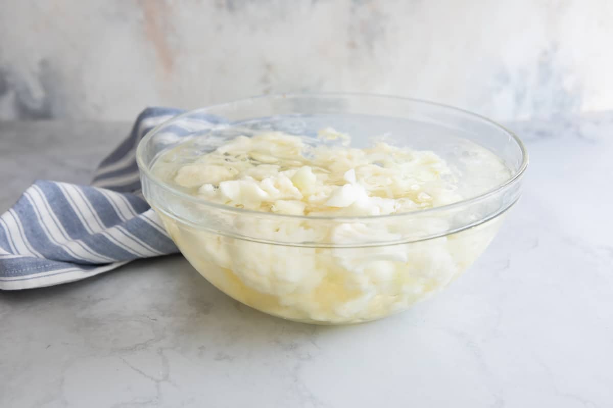 Cauliflower florets in a glass bowl of ice water.