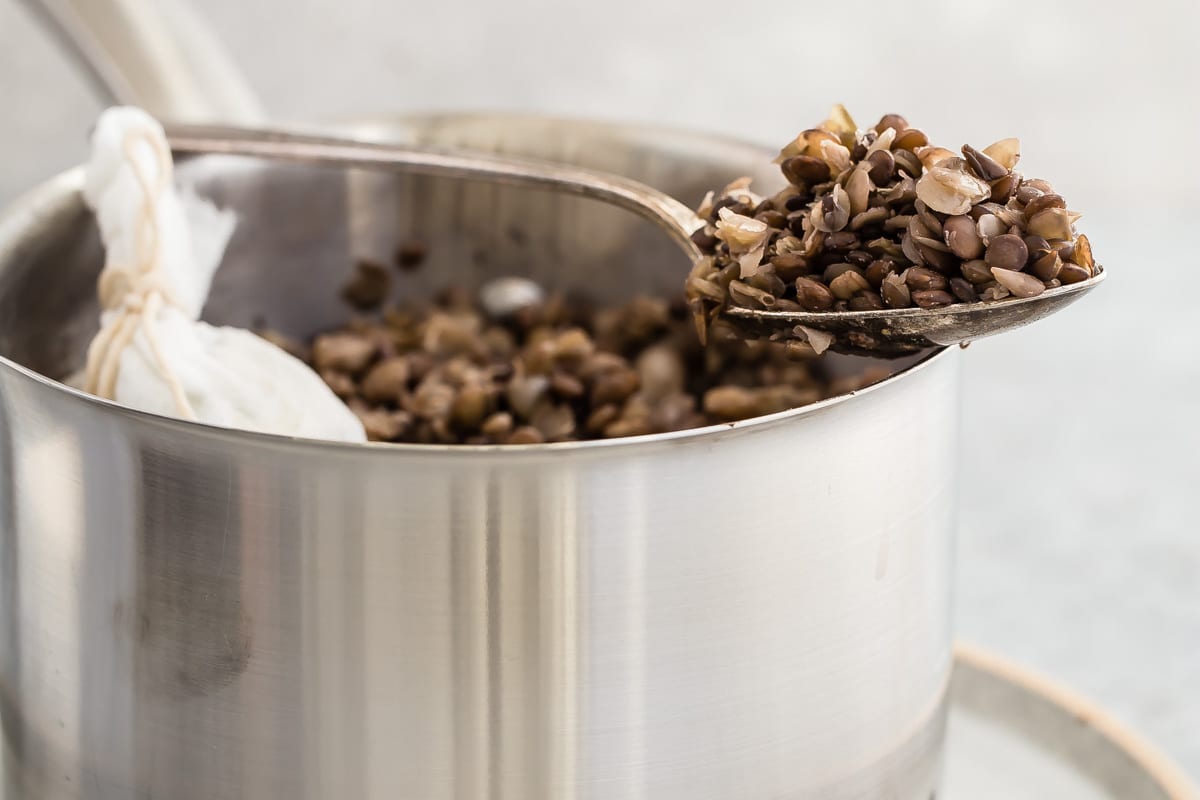 Cooked lentils in a silver pot with some in a spoon resting on the edge of the pot.