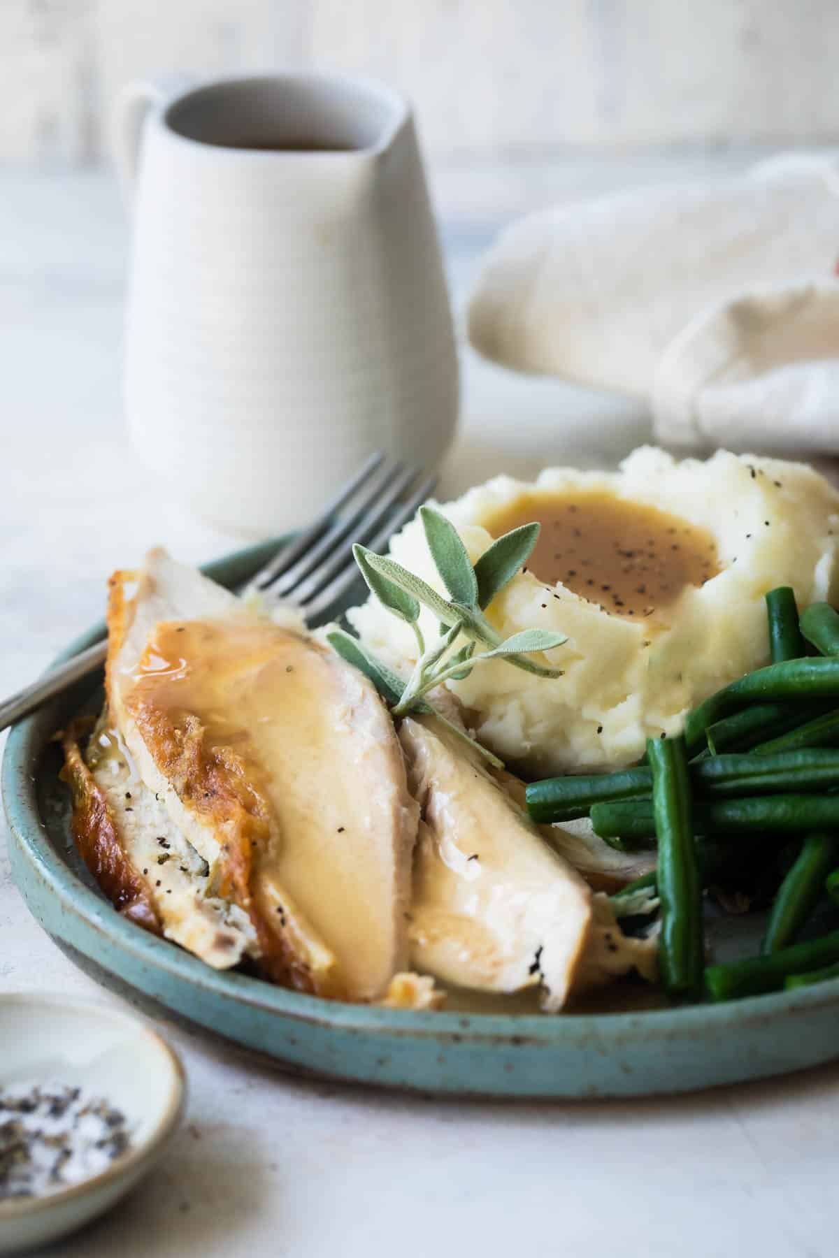 A plate of roast chicken with mashed potatoes, gravy, and green beans.