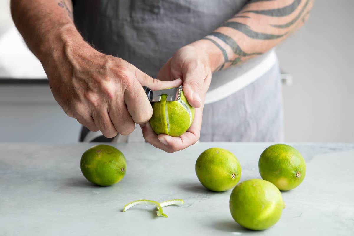 Someone zesting a lime with a zesting tool.