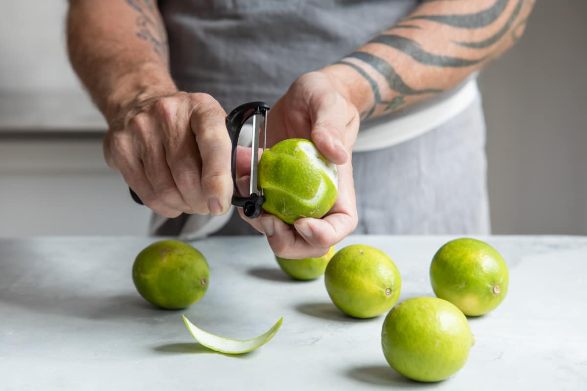 Someone peeling a lime with a peeler.