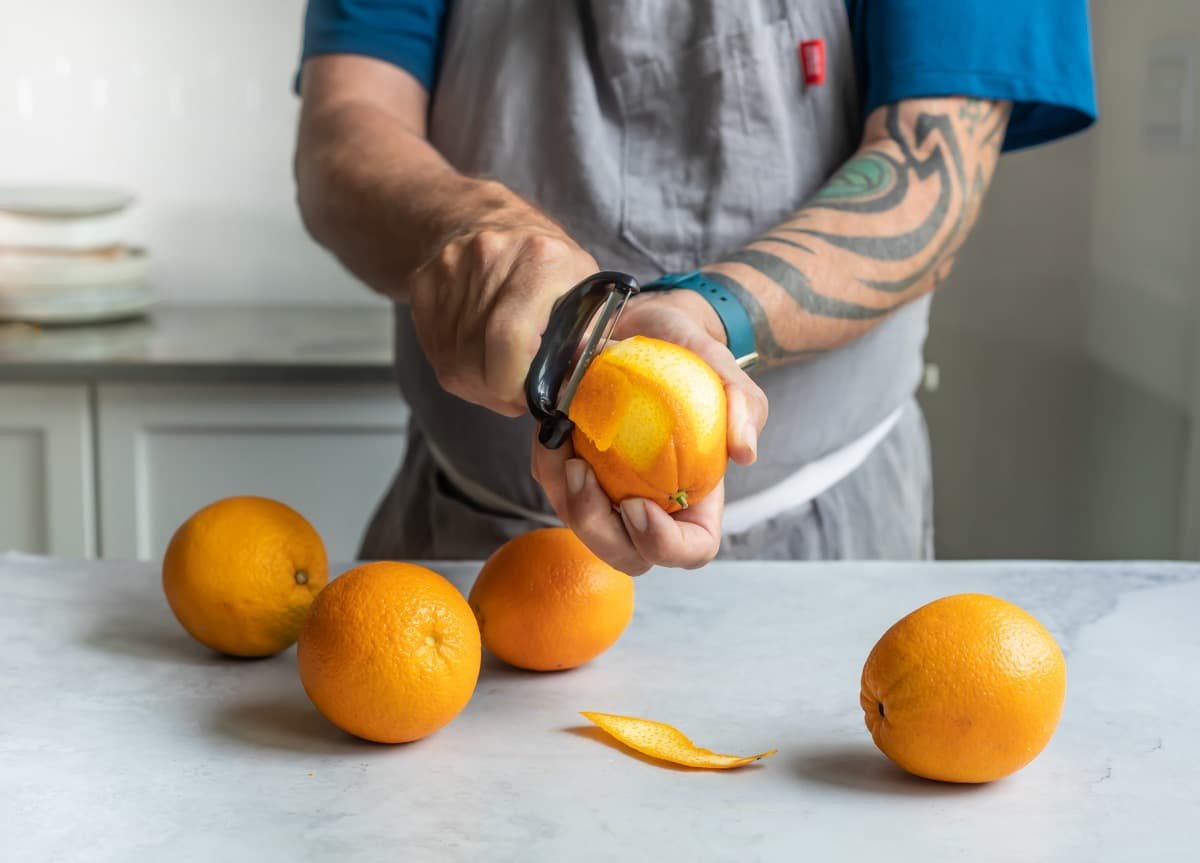 Someone peeling an orange with a peeler.