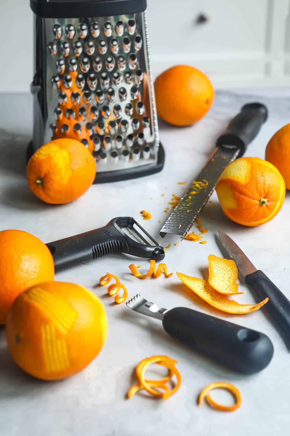 Five oranges on a countertop that have been zested with various tools.