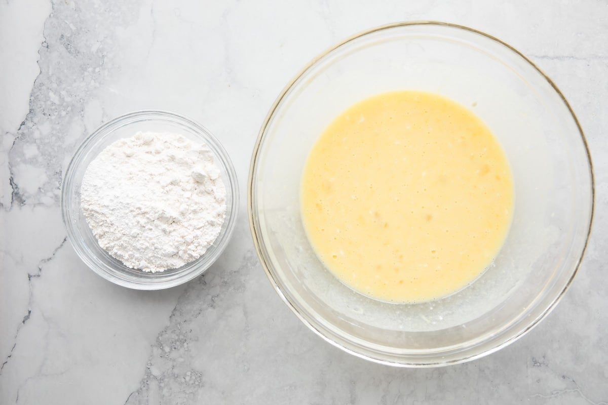 Lemon yogurt cake dry ingredients in a glass bowl next to lemon yogurt cake wet ingredients.