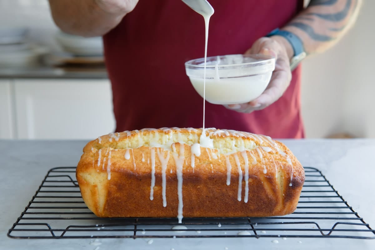 Someone drizzling icing on a lemon yogurt cake.