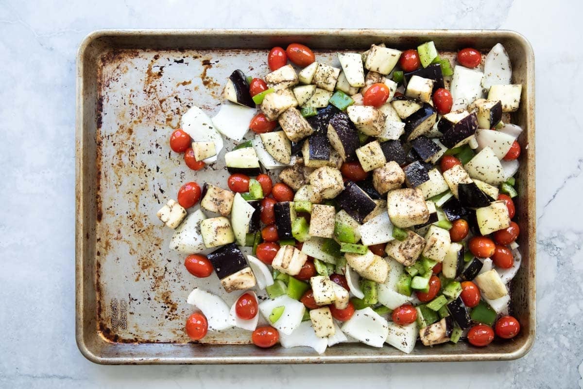 Eggplant, tomatoes, onions, and peppers on a sheet pan.